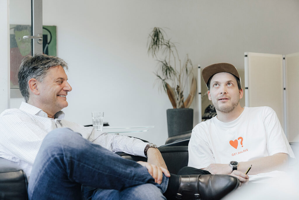 Joachim Hornegger und Simon Reif sitzen gemeinsam auf einem Sofa und reden miteinander.