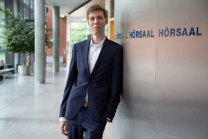 Prof. Dr. Benedikt Downar lehnt an einer Wand auf der Hörsaal steht