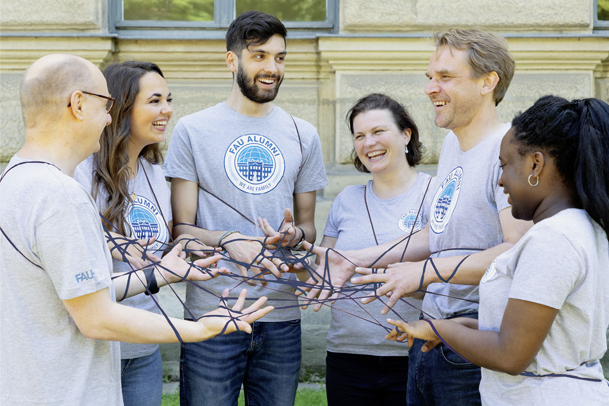 Mehrere Menschen stehen im Halbkreis und sind mit einem blauen Band verbunden.