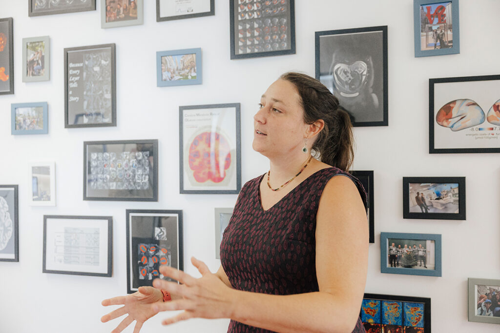 Prof. Hutter steht vor einer Bilderwand, sie ist nach links gedreht und erklärt einer nicht sichtbaren Person etwas.