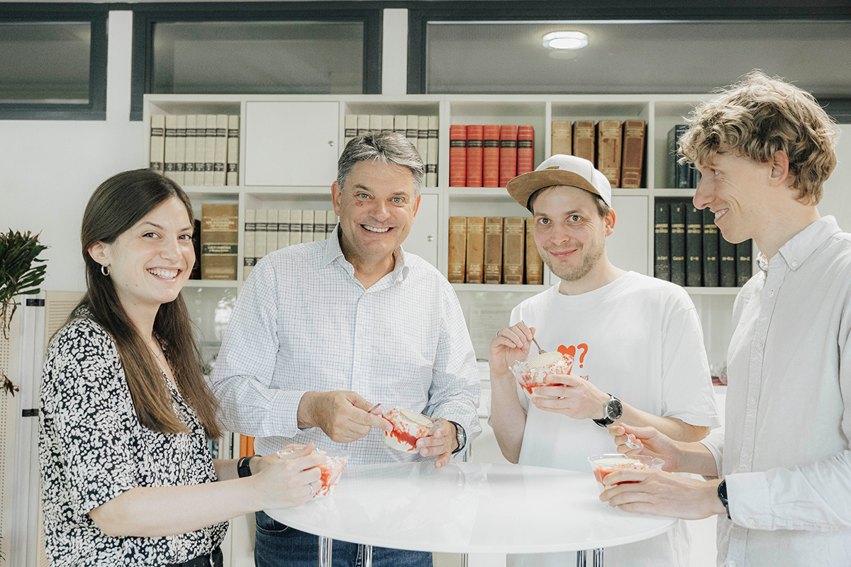 Der FAU-Präsident Hornegger, Prof. Dr. Reif und das Team von Prof. Reif stehen gemeinsam um einen Tisch herum und essen Spaghettieis.