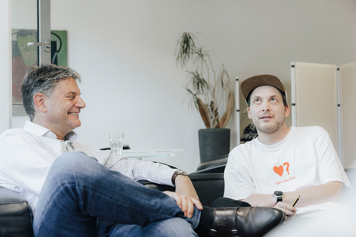 Joachim Hornegger und Simon Reif sitzen gemeinsam auf einem Sofa und reden miteinander.