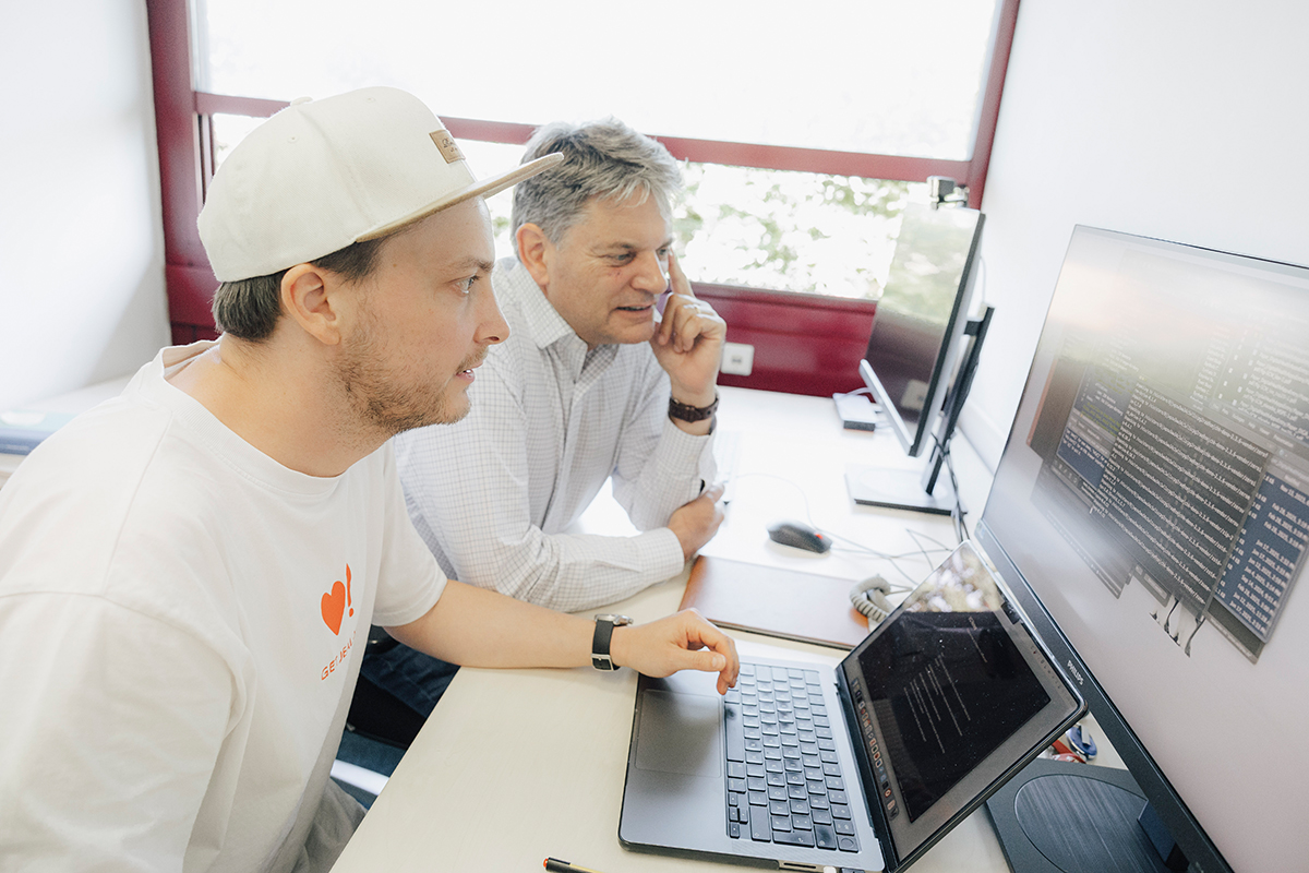Hornegger und Reif sitzen gemeinsam vor einem Laptop und einem Bildschirm und betrachten sie.