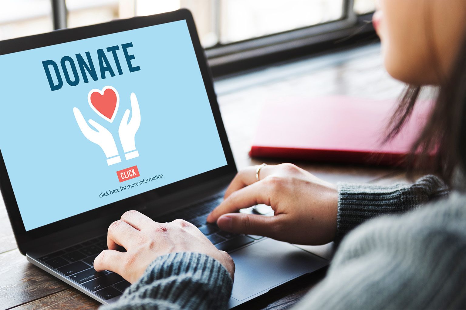 Eine Person auf einem Laptop der Bildschrim zeigt das Wort "Donate" und Hände, die ein Herz halten
