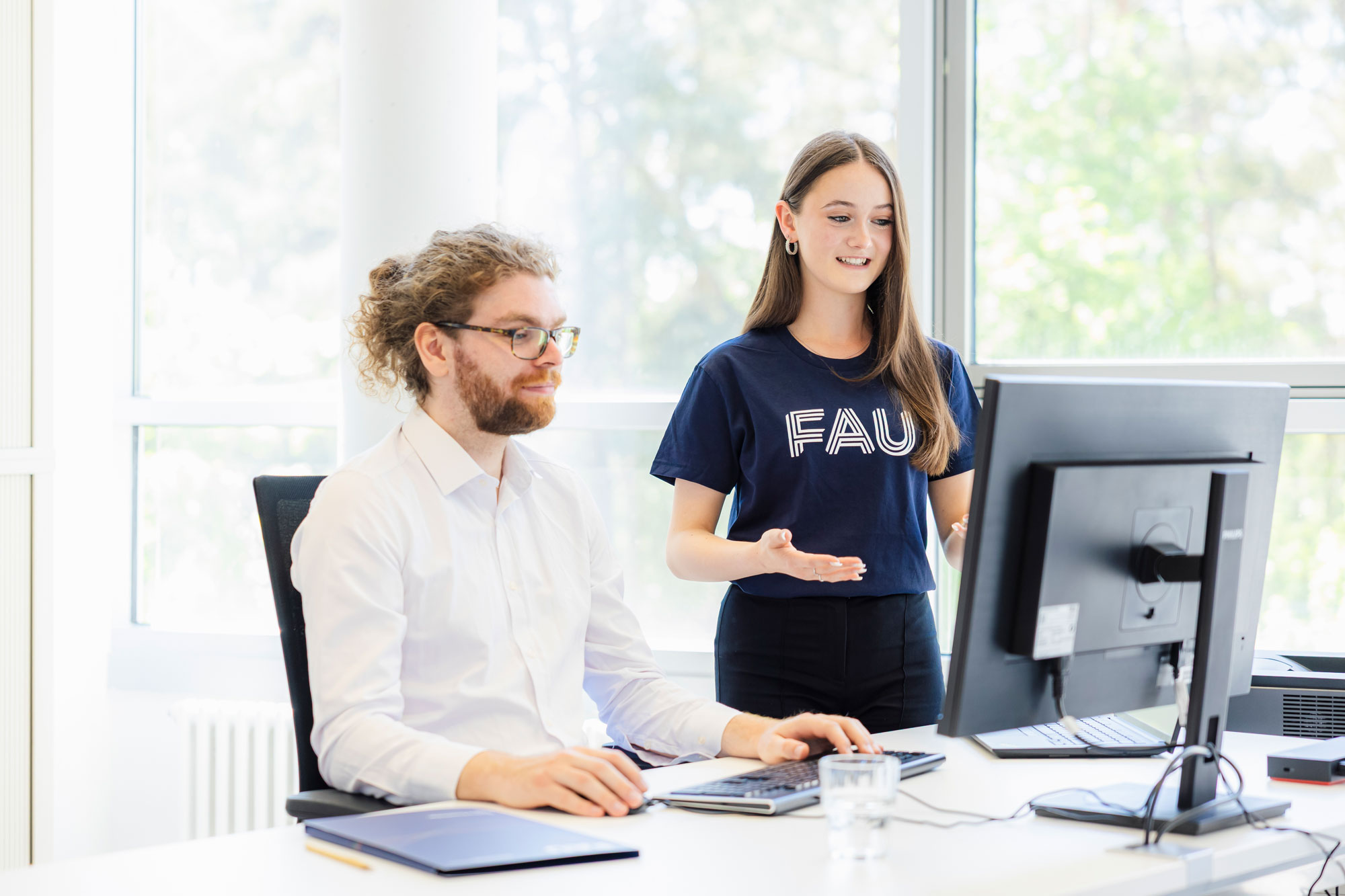 Eine Frau spricht mit einem Mann vor dem PC