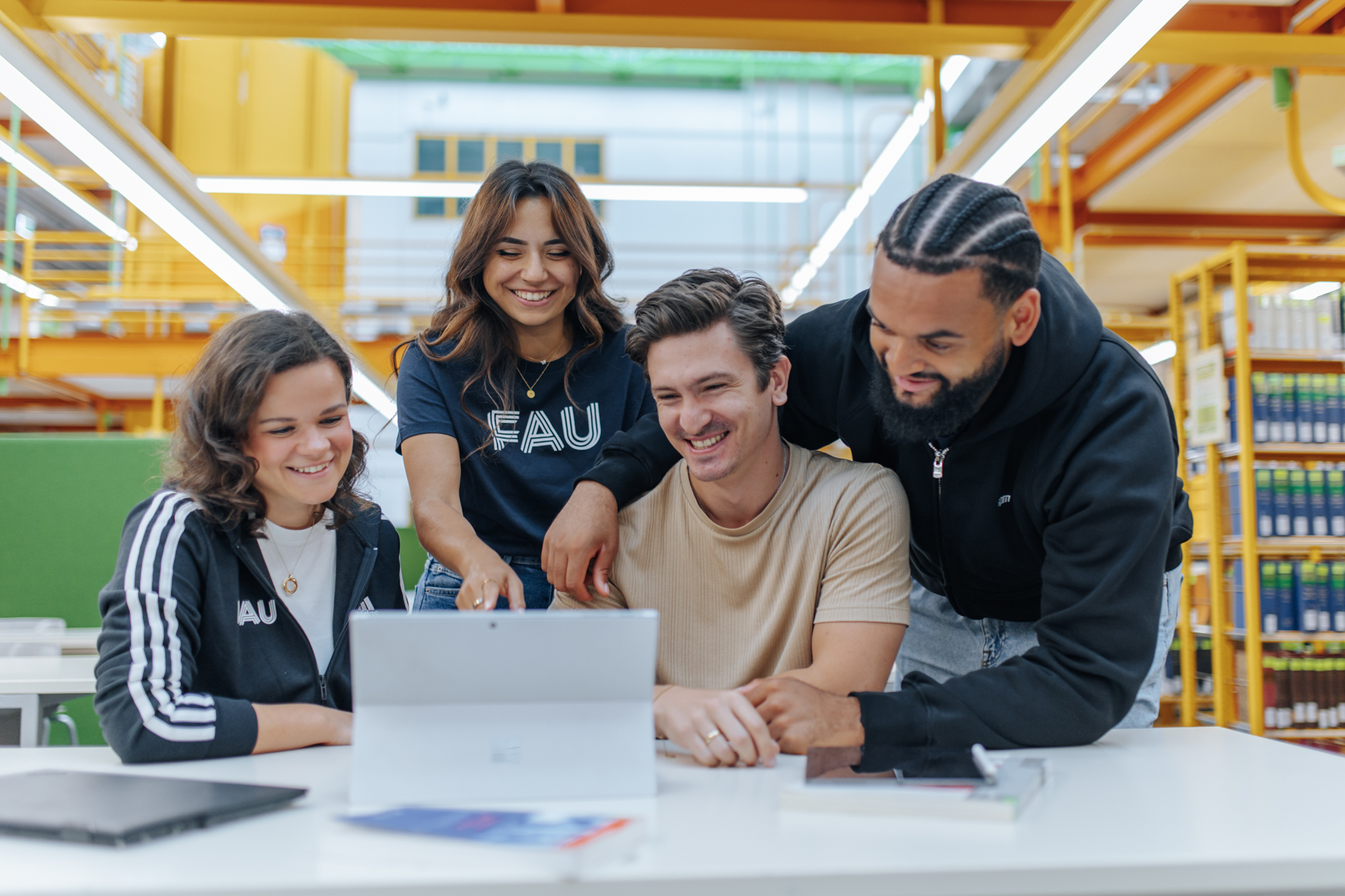 Vier Studierende in der Bibliothek schauen in ein Laptop.