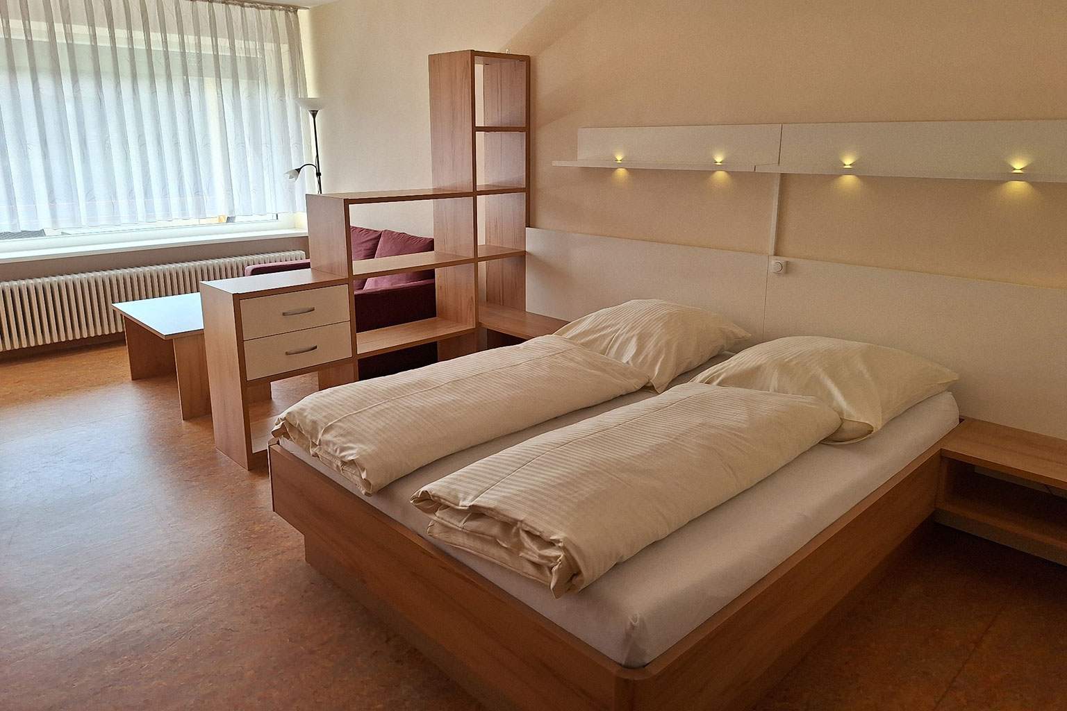 View of a room with double bed, shelves and a couch.