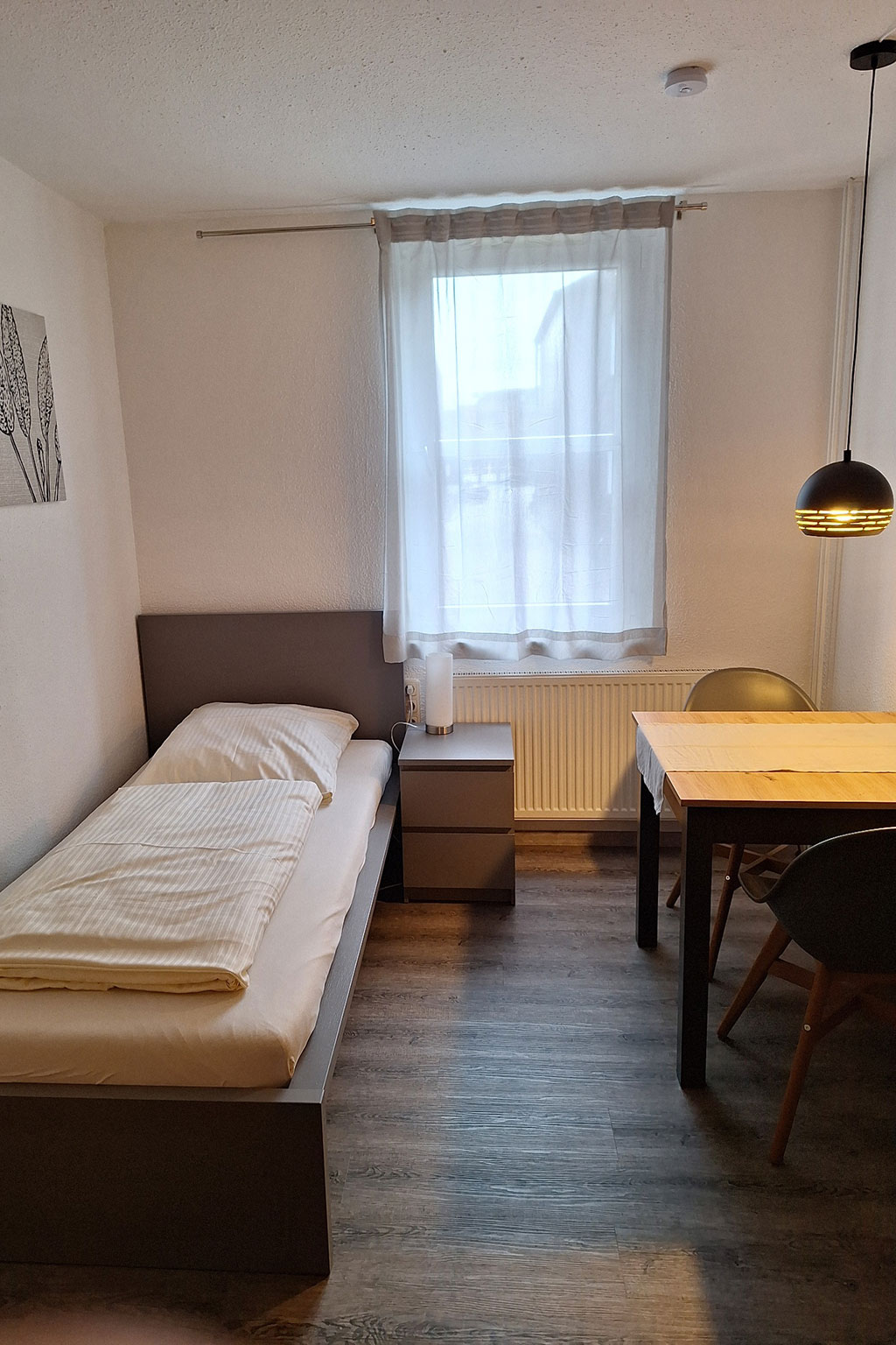 View of a single room with bed and table.