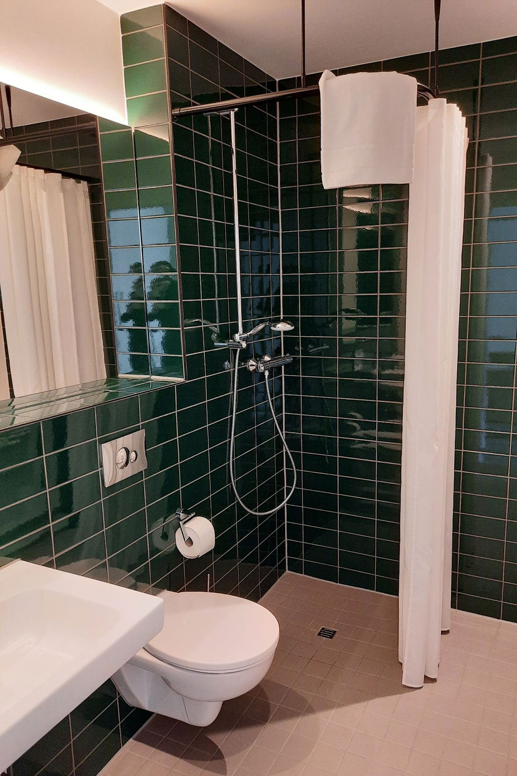 View of a bathroom with green tiles.