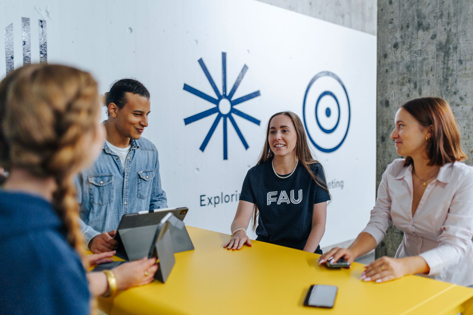 Mehrere Personen sitzen mit Tablets, Laptops und Handys zusammen am Tisch.