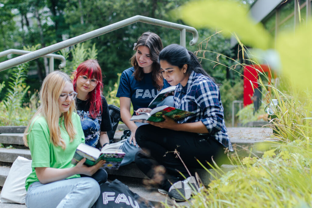 Studierende sitzen auf einer Treppe und schauen in eine Broschüre