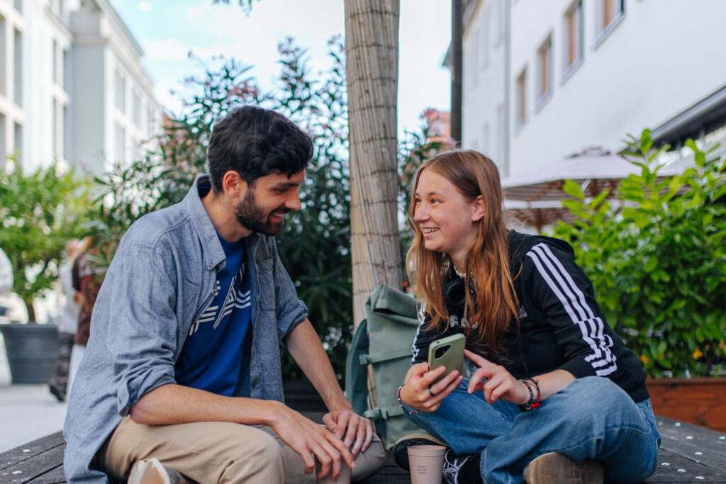 Ein Mann und eine Frau sitzen auf einer Bank und schauen auf ein Smartphone