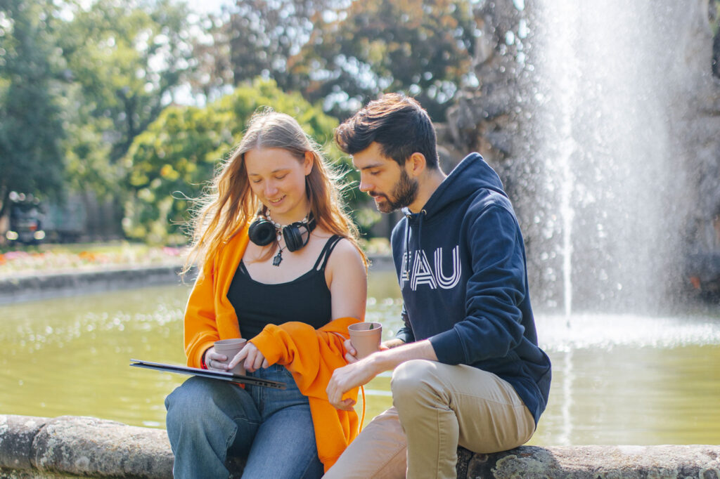 Zwei Personen sitzen vor dem Brunnen und schauen auf ein Tablet