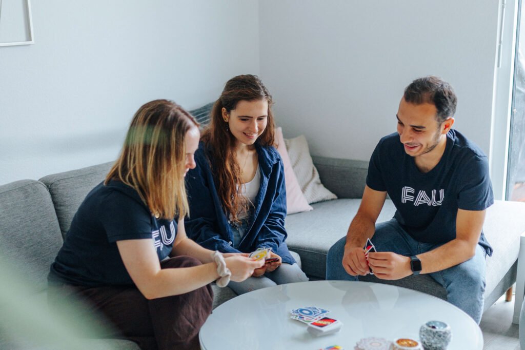 Drei Personen spielen an einem Couchtisch ein Kartenspiel.