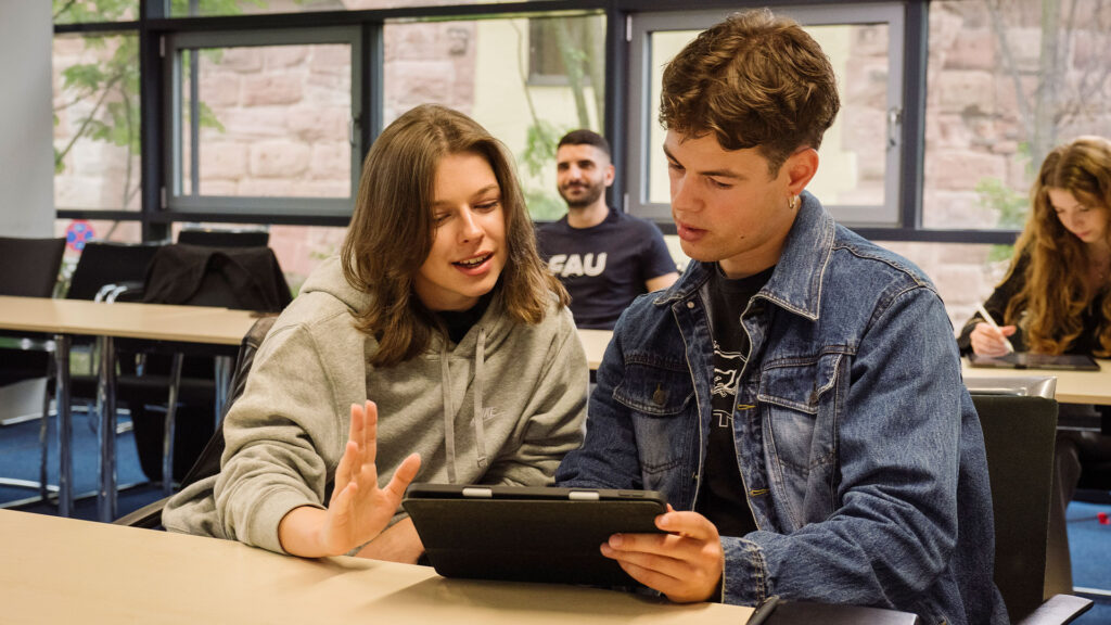 Zwei Studierende arbeiten gemeinsam an einem Tablet.