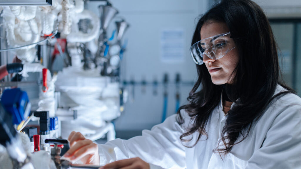 Eine Forscherin mit Schutzbrille und Kittel arbeitet an ihren Geräten.