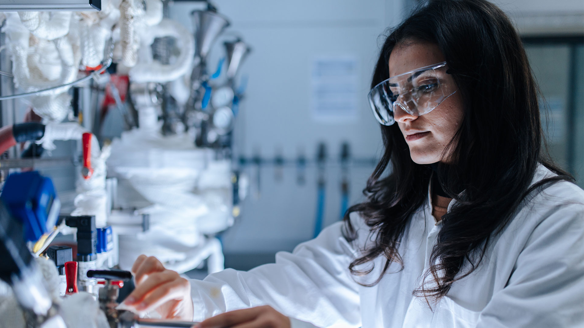 Eine Forscherin mit Schutzbrille und Kittel arbeitet an ihren Geräten.