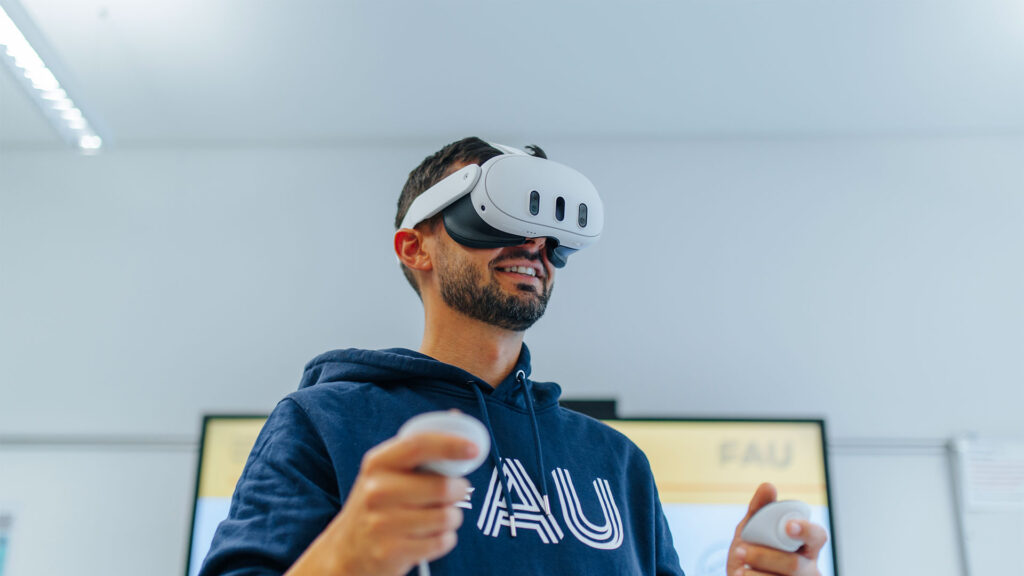 Ein Mann mit VR-Brille und FAU-Hoodie.