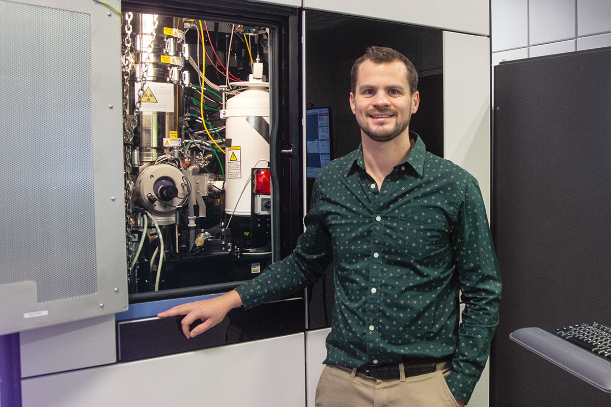 Pelz, ein junger Prof, mit braunen Haaren, einem kurzen Bart, trägt ein grünes Hemd, vor einer Maschine.