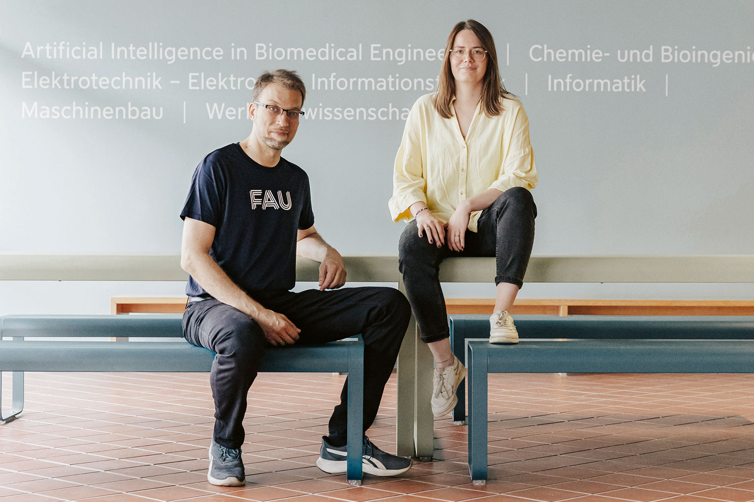 Ein Mann und eine Frau sitzen auf Bänken und einem Geländer.