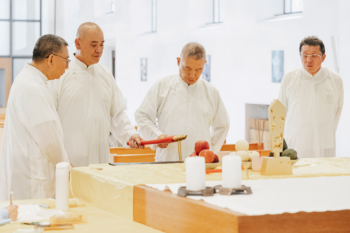 Drei Männer in weißen Roben mit einem Gerät aus rotem Holz an einem Altar.