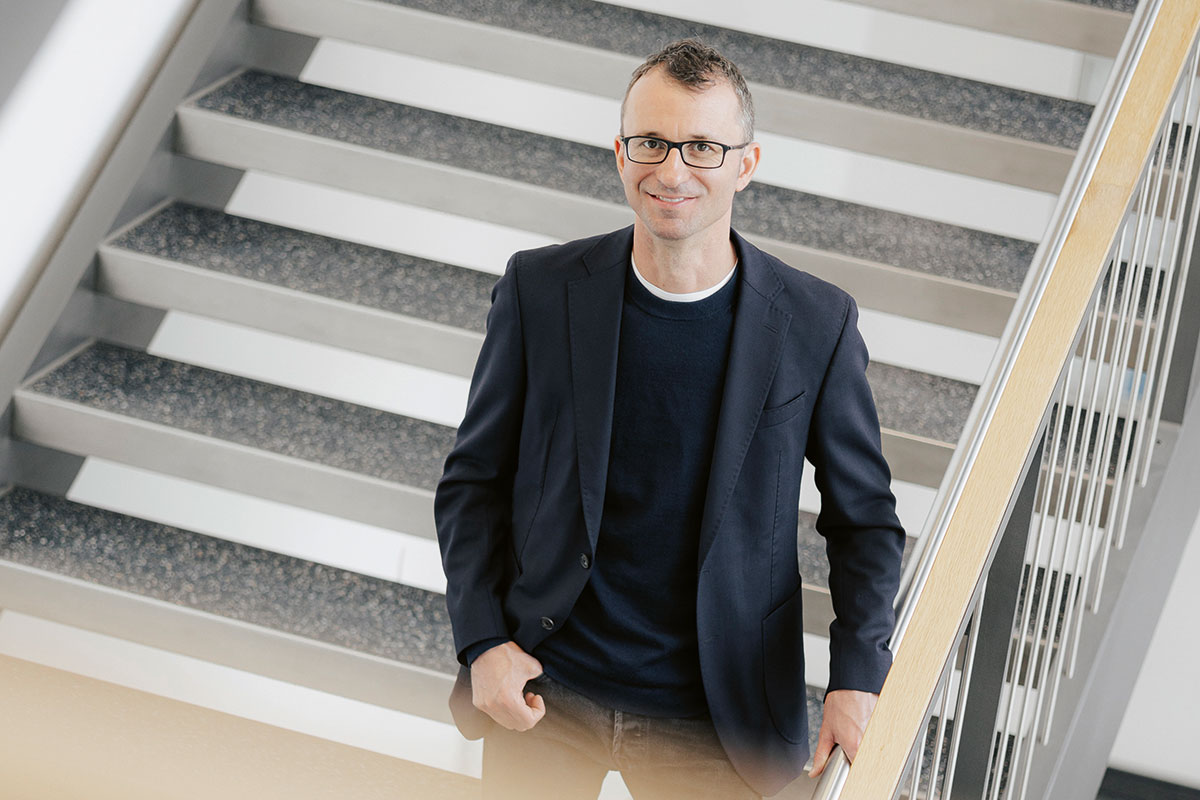 Dr. Wieland, ein Mann mit Brille, geheimratsecken und im schwarzen Jacket, lächelt aus der Vogelperspektive in die Kamera.