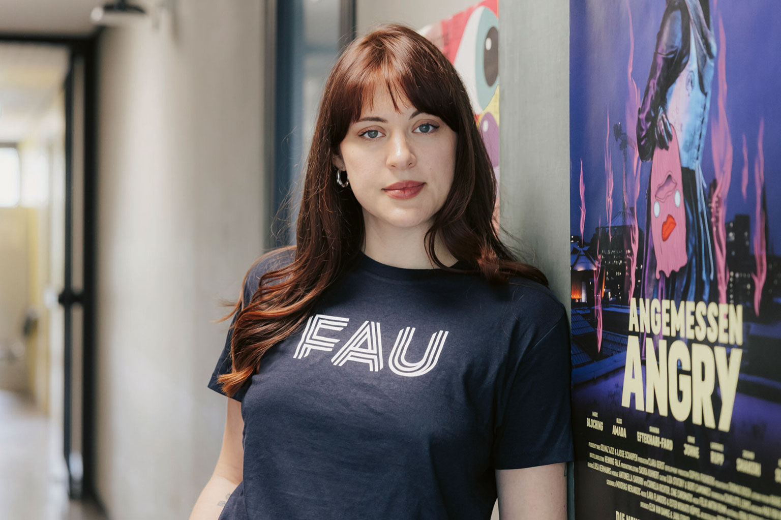 Jana Forkel im FAU-Shirt vor einem Filmplakat.