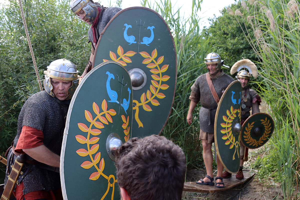 Männer in römischer Soldatenuniform und Schilden steigen in ein Boot.