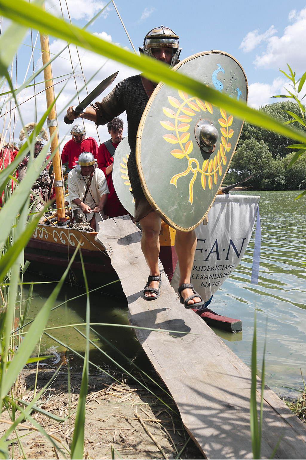 Männer in roten Tunikas und römischen Uniformen rennen einen Landungssteg an Land.