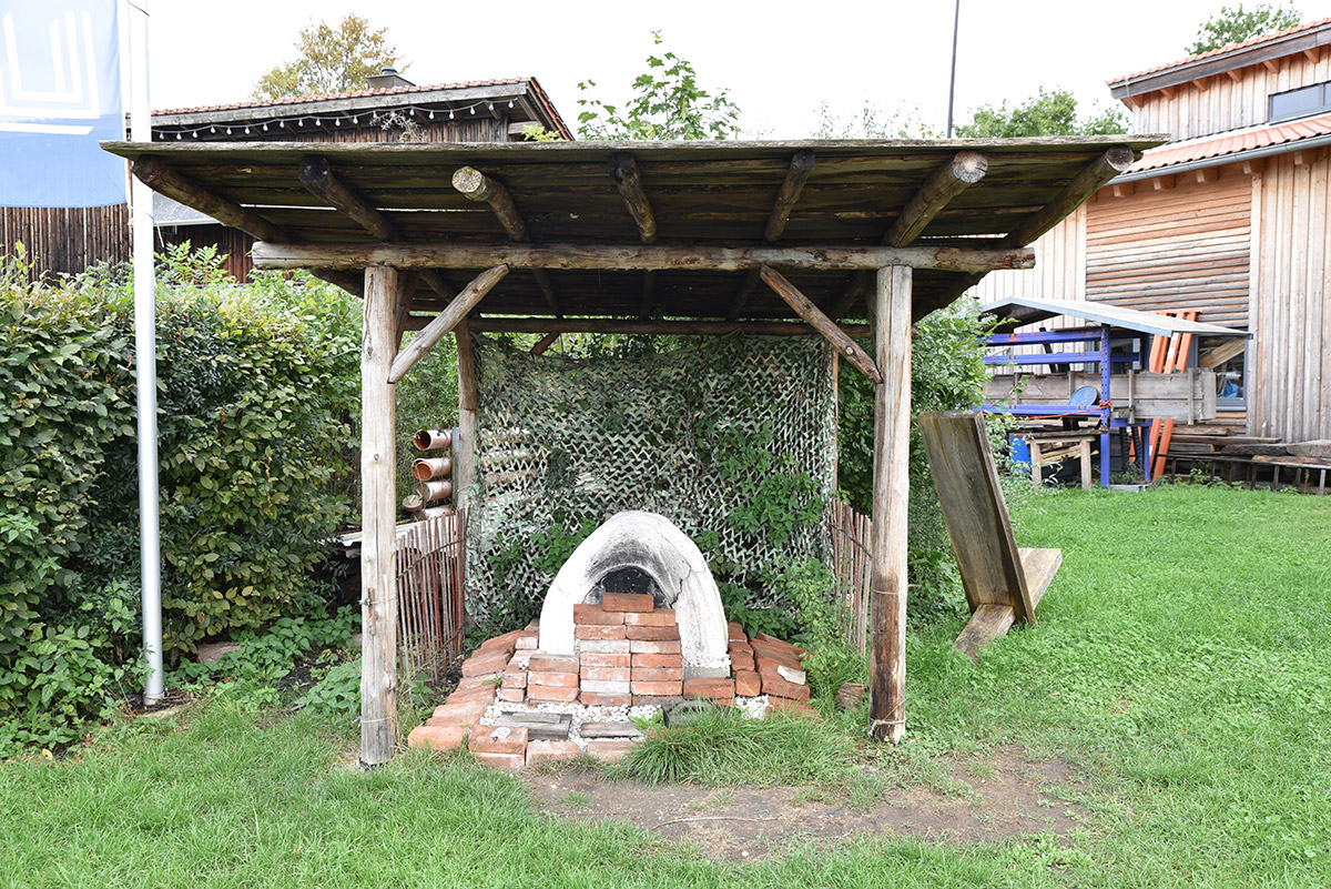 Unter einem Holzdach steht ein Ofen.