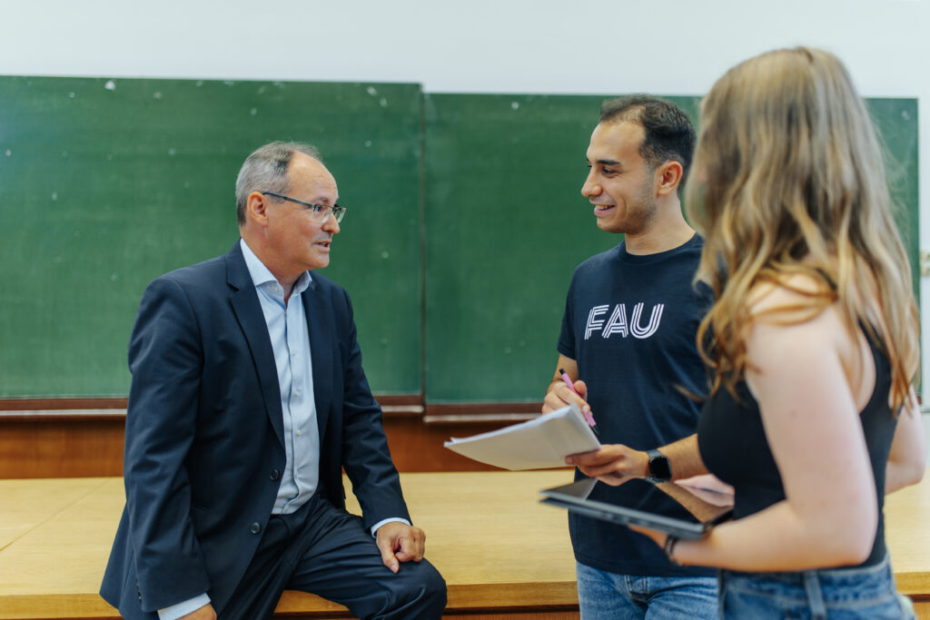 Drei Personen besprechen sich in einem Hörsaal.