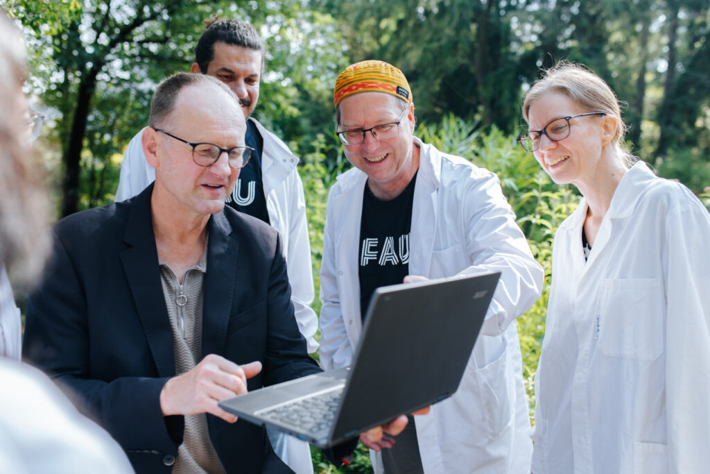 Fünf Personen schauen gemeinsam auf ein Laptop in einem Garten.