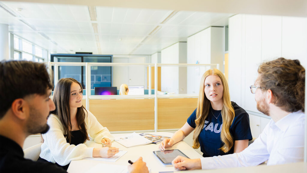 Eine Gruppe von jungen Menschen bespricht sitzend an einem Tisch.