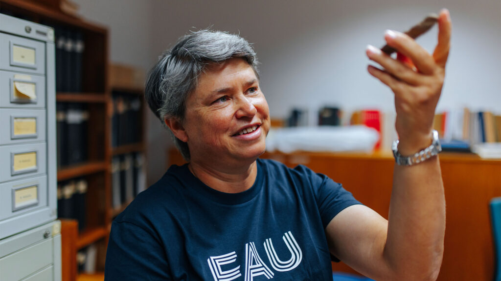 Ein etwas ältere Forscherin hält einen alten Stein in die Luft und betrachtet ihn.