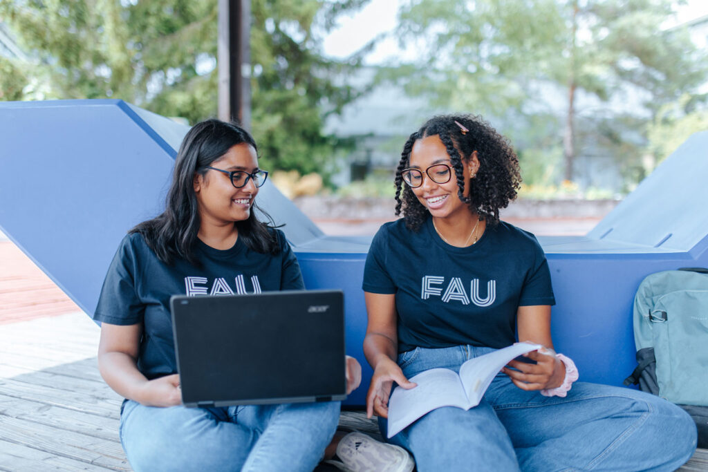 Zwei Studentinnen sitzen in einem Außenbereich und besprechen sich.