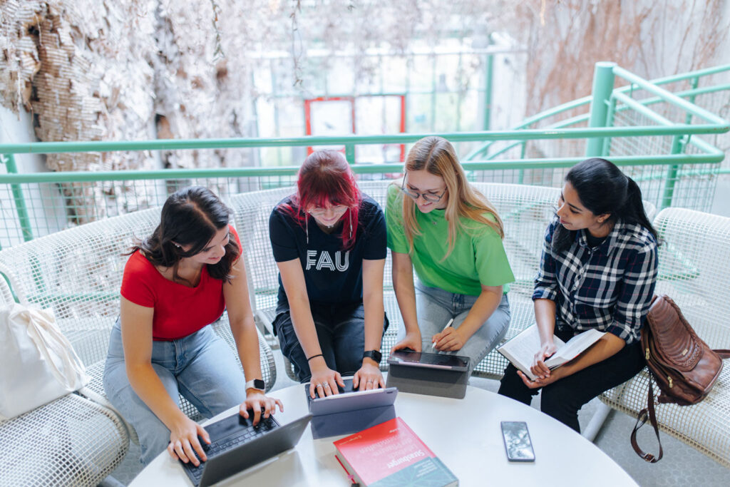 Vier Studentinnen sitzen auf einer Bank und schauen in Laptops.