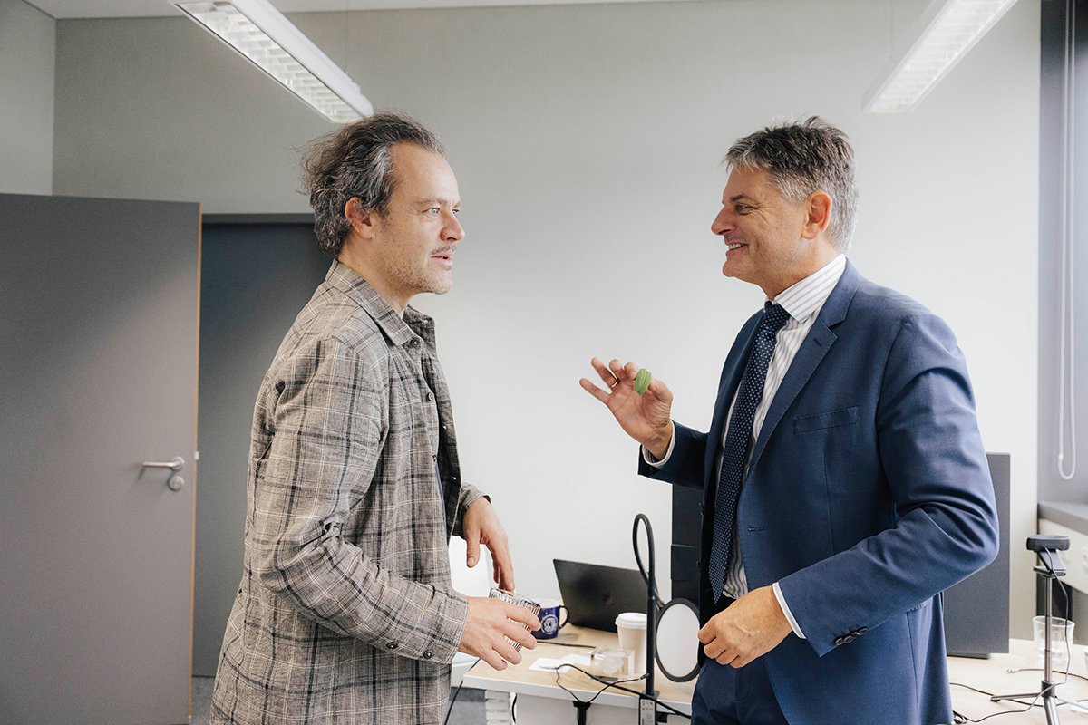 Hornegger and Riedl stand opposite of each other and talk. Hornegger holds up a green macaron.