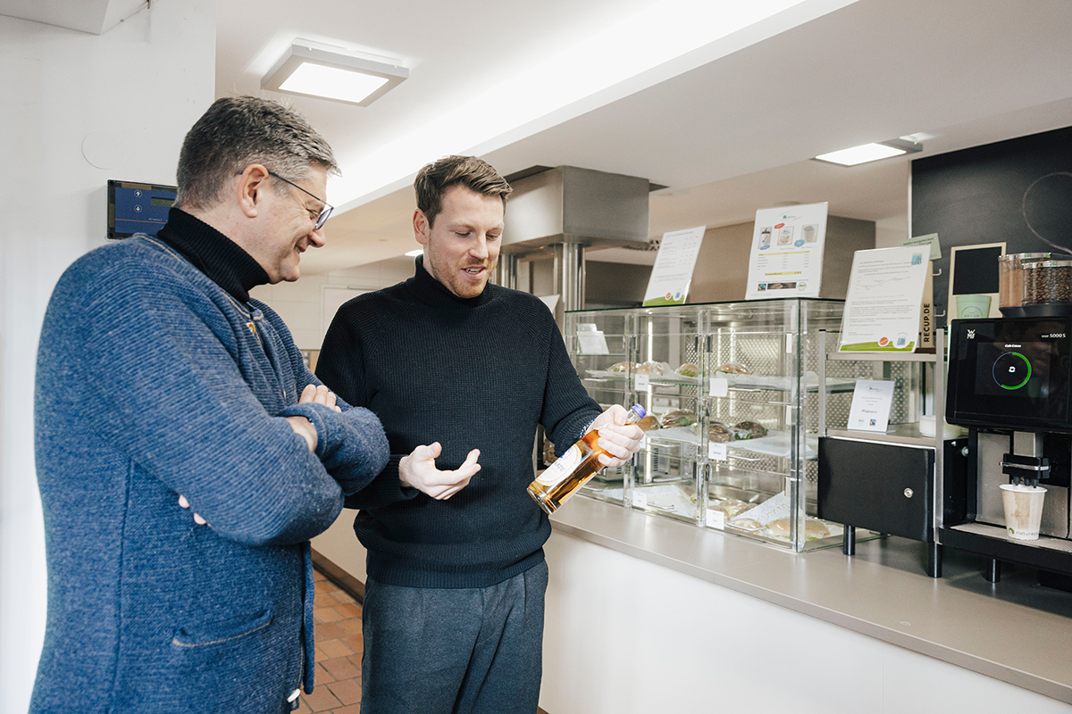 Hornegger and Nipper are standing next to each other in the cafeteria, looking at a bottle.