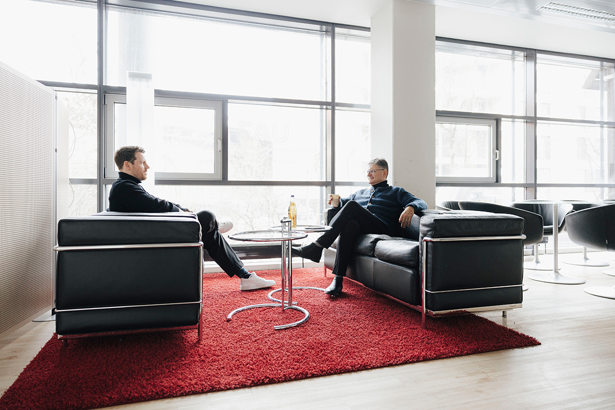 Professor Nipper and President Hornegger sit facing each other on two sofas in a bright office.