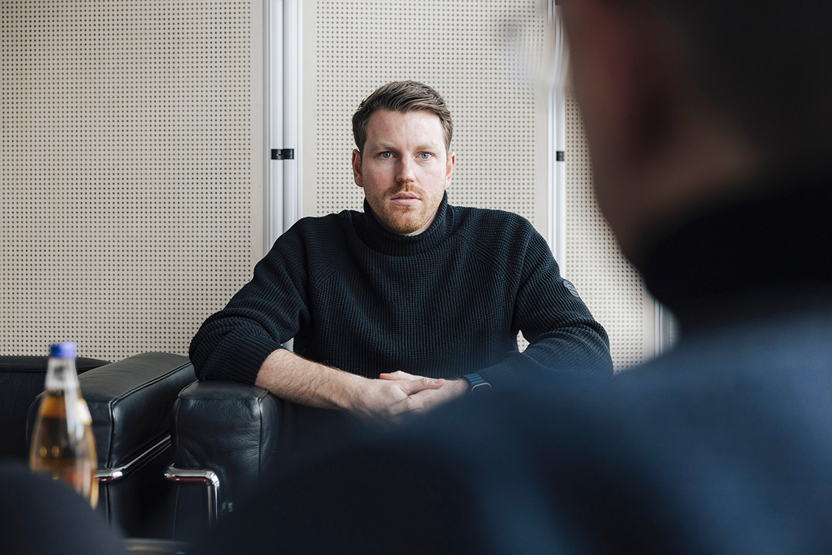 A portrait photograph of Marvin Nipper. He is looking directly at the camera, with the blurry outline of a man visible in the foreground on the right.