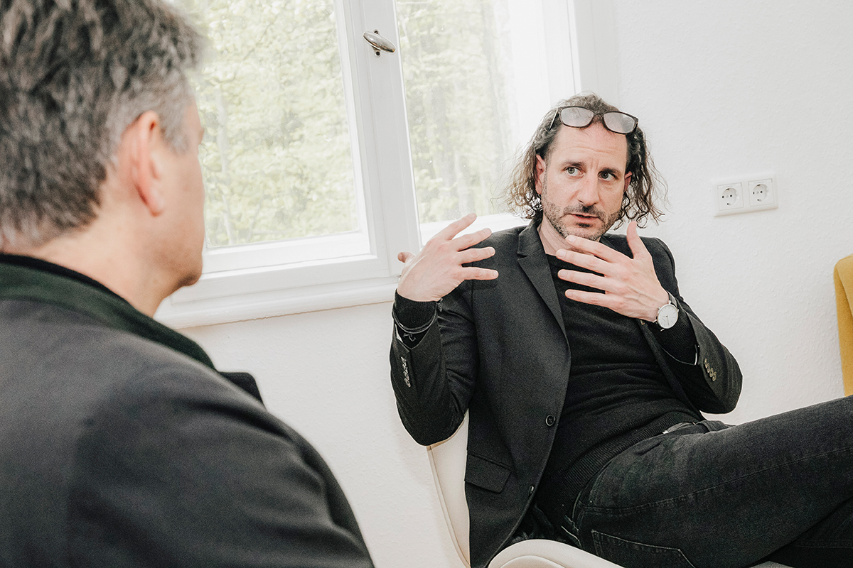 Hornegger is sitting with his back to the camera, his silhouette is visible at the left hand side of the picture. Maltese is sitting opposite him and looking at him while explaining something using gestures.