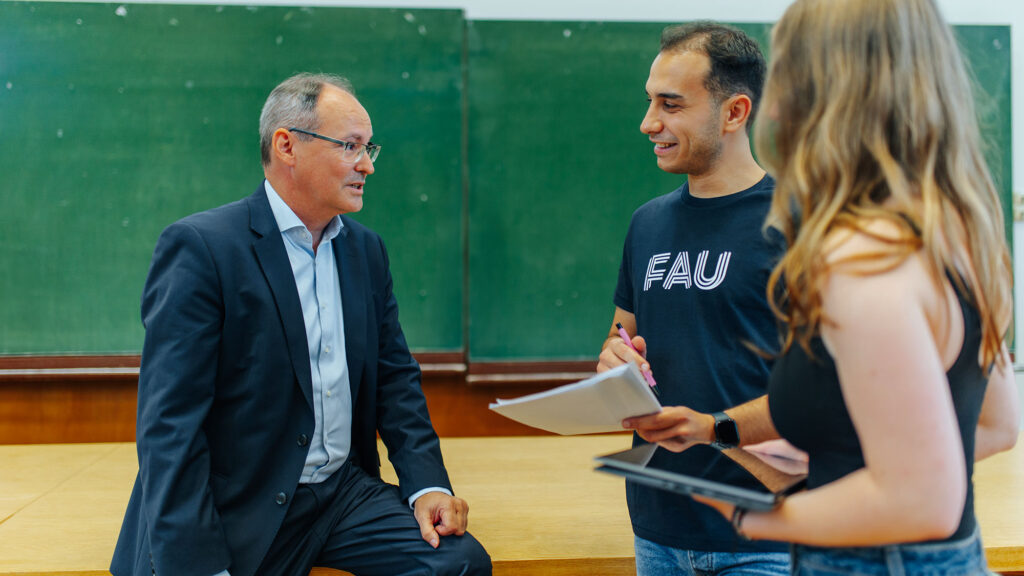 Drei Personen besprechen sich in einem Hörsaal.