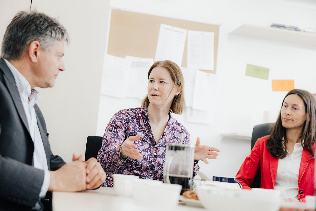 Schilling-Vacaflor, Hornegger and another woman are sitting at a table. Schilling-Vacaflor is explaining something, gesturing and looking at Hornegger.